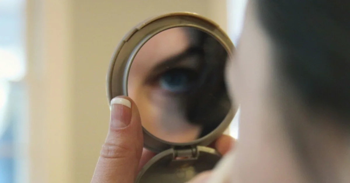A person applying quick everyday makeup in front of a mirror