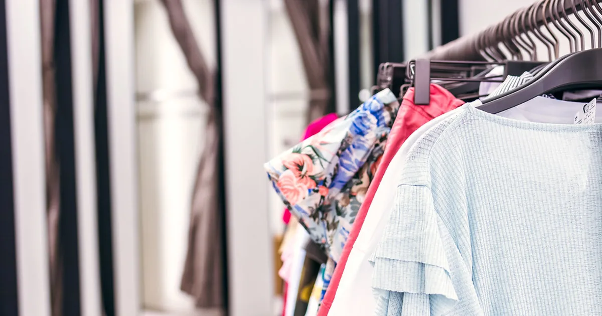A rail of folded shirts and jackets arranged by colour in a wardrobe